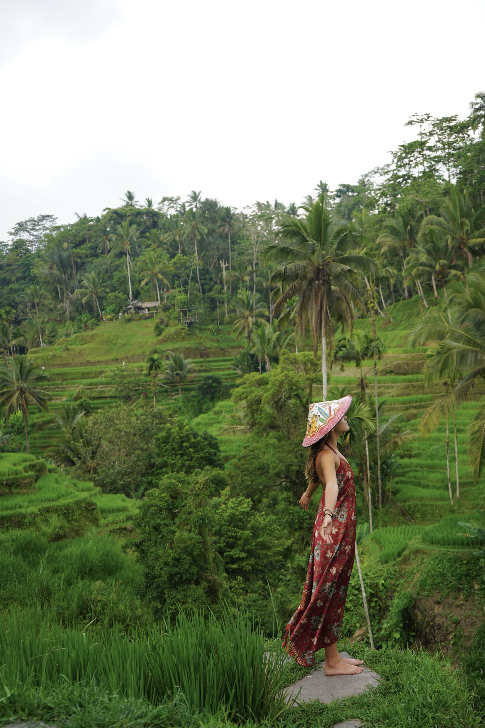Una mujer con sombrero cónico y vestido rojo, de pie frente a los arrozales en terrazas de Bali